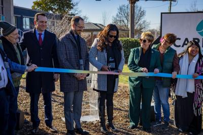 A row of people stand behind a rainbow colored ribbon, a woman in the center holding scissors