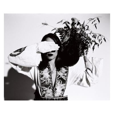 Cover art for Anana Kaye’s album ‘Are You There,’ featuring a black and white photo of the artist with her left hand holding a bouquet of flowers behind her head and her right hand over her eyes, palm out