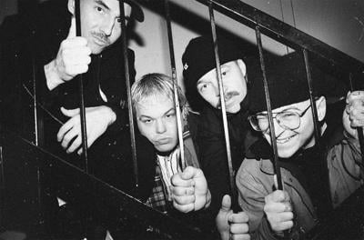 Black-and-white photo of Beton Arme with the band posing behind stair railing resembling bars of a jail cell