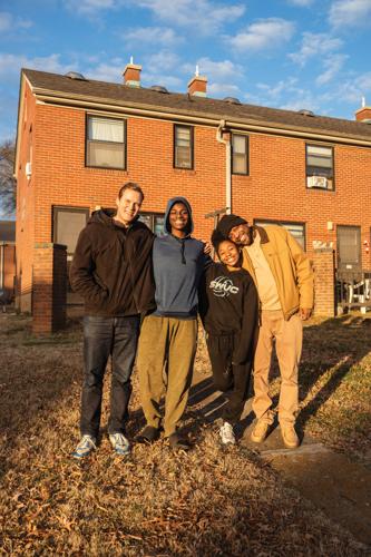 Four people stand in front of a brick building smiling