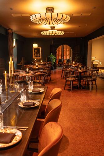 A woden bar with three seats and a few tables inside of a restaurant.