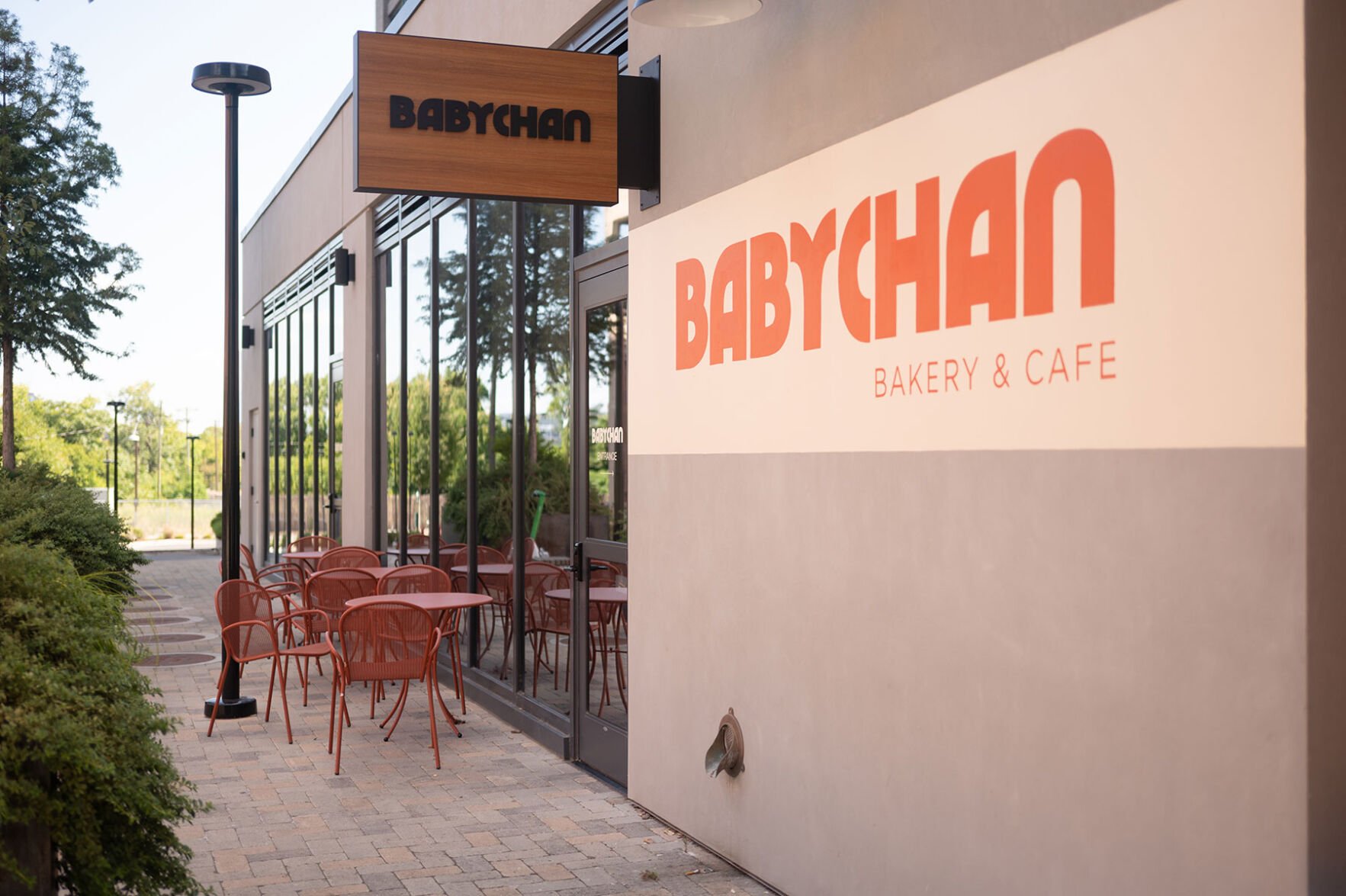 The exterior of a building whose wooden sign reads "Babychan." A yellow stripe along the pink wall also reads "Babychan Bakery and Cafe"