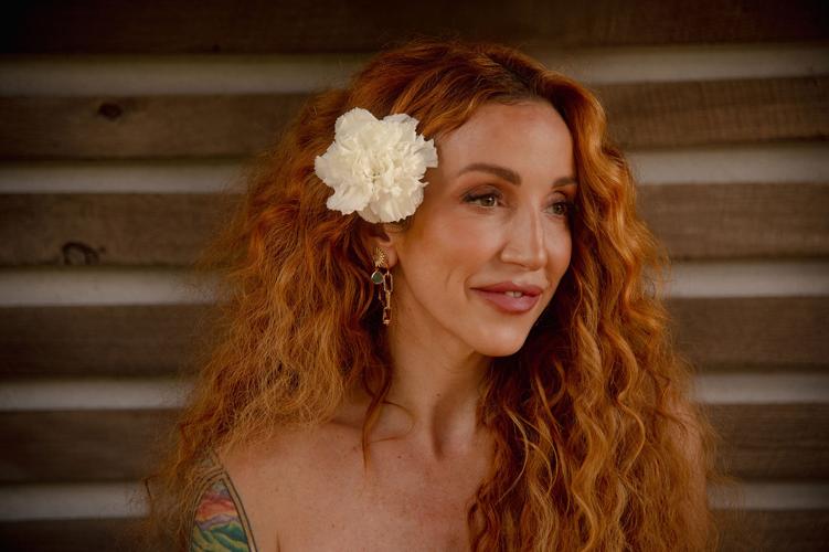 Ashley Monroe press photo 2025 artist stands against a weathered wooden wall with a white flower in her hair
