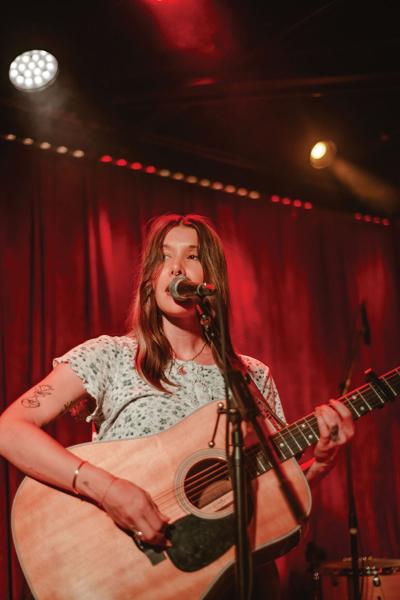 Color photo of Bre Kennedy, the Nashville Scene’s 2026 Best Singer-Songwriter, singing into a microphone and playing an acoustic guitar
