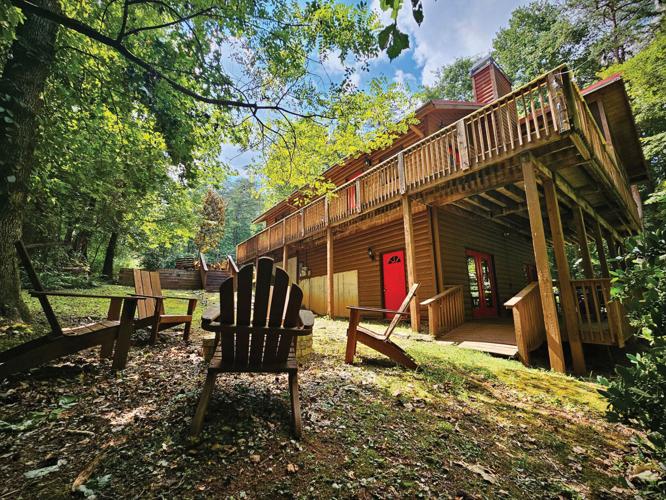 A two story cabin in the woods with patio furniture in the foreground.