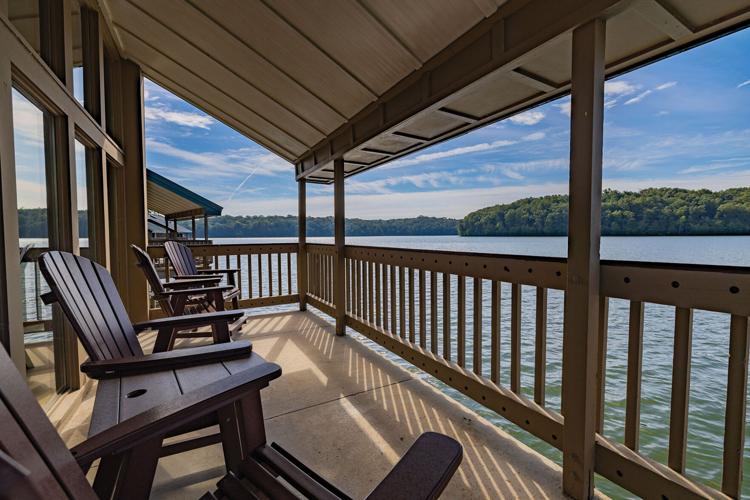 Adirondack chairs in a row on a deck jutting out over a lake.