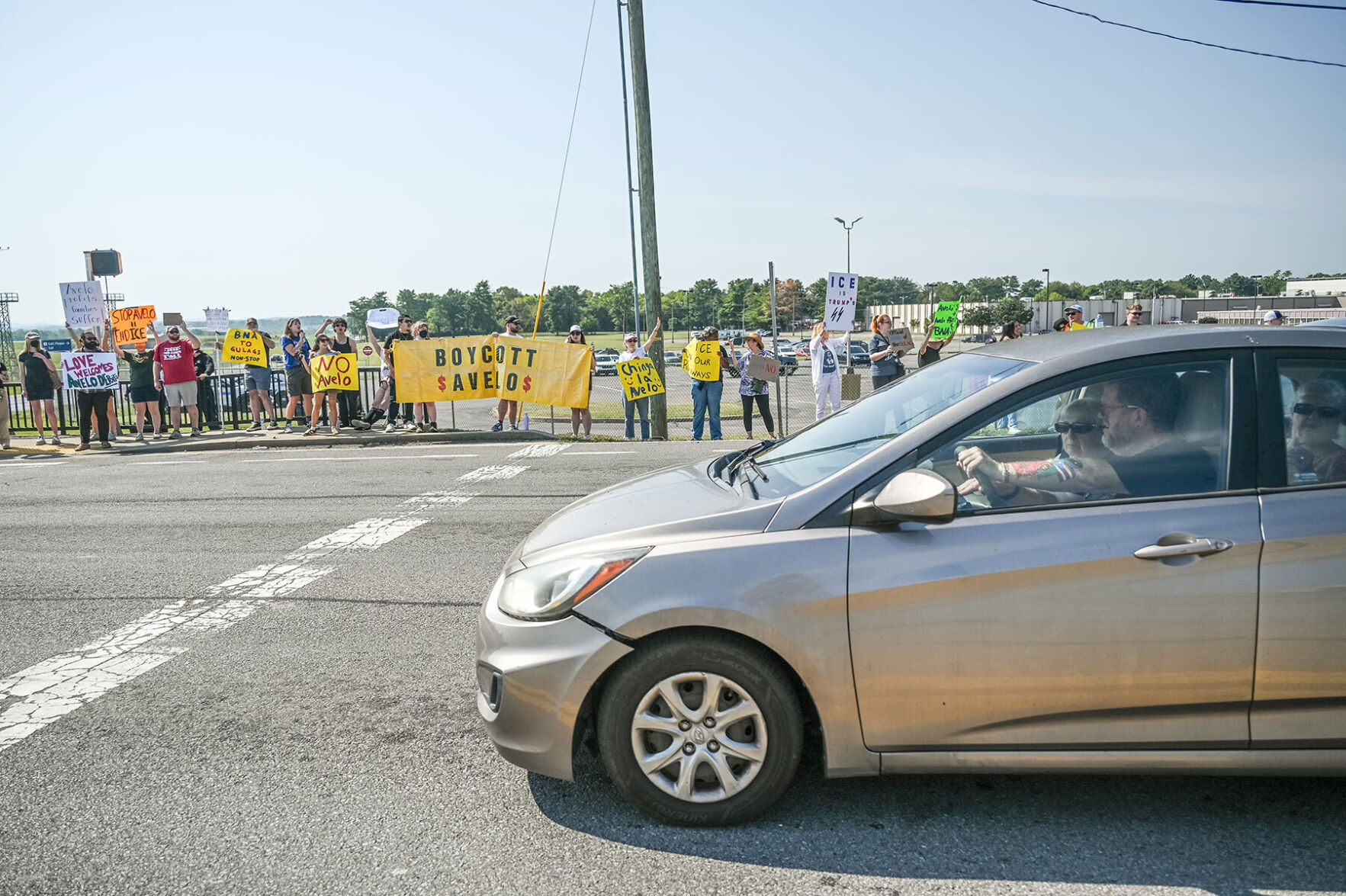 A car drives by protesters waving signs calling for a boycott of Avelo