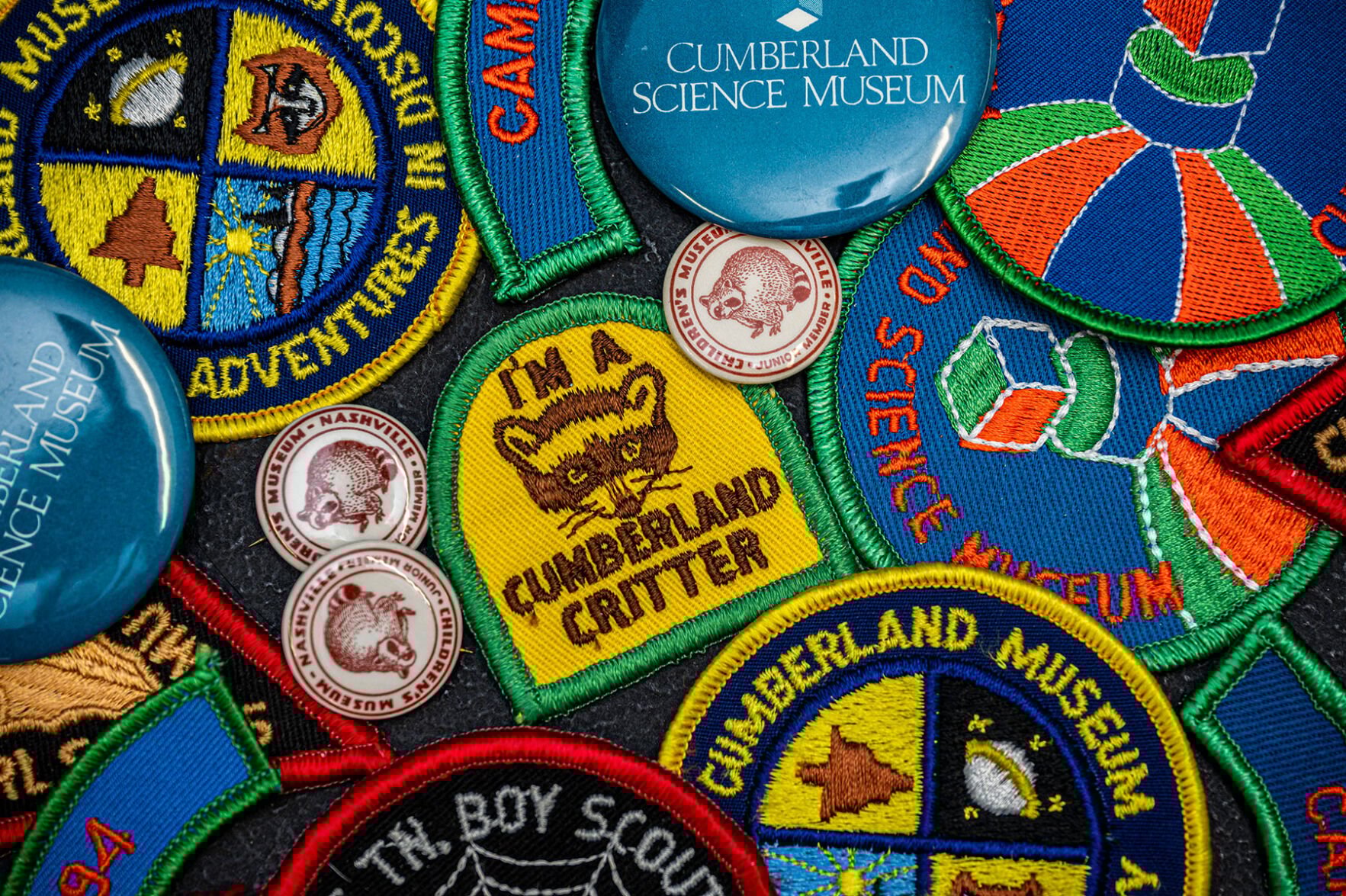Various colorful patches; in the center is a yellow one featuring a raccoon's face and the words "I'm a Cumberland critter"