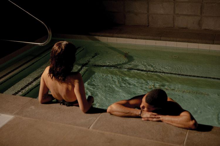 A woman and a man recline at the edge of a pool