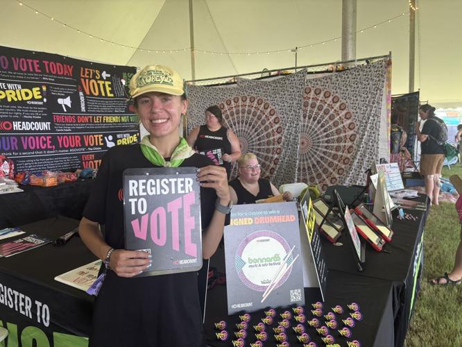 Color photo of volunteers at the table operated by voter registration organization Headcount at Bonnaroo, 2026. A volunteer holds up signage reading “Register to Vote.”