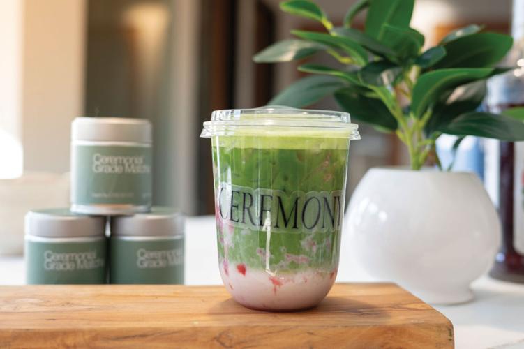 A matcha latte with strawberry syrup sits on a wooden board, a label reading "ceremony" stuck to the transparent cup