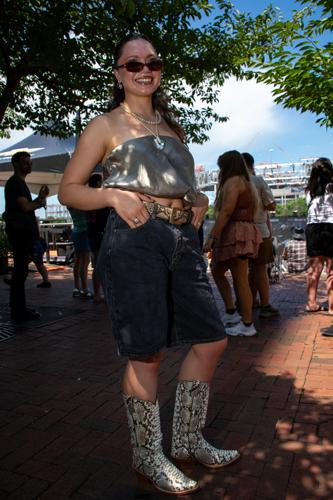 Color street style portrait of CMA Fest fan Caroline Stelte, sporting black jorts, tiny sunglasses and other hallmarks of social media trends, paired with fancy cowboy boots.