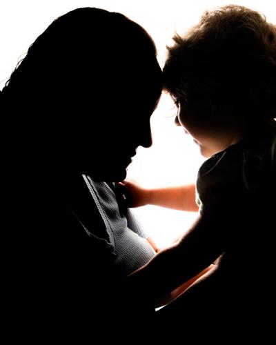 A woman holds a 2-year-old girl up to her face, the features of both figures hidden by shadows
