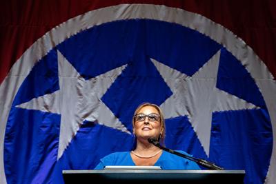 Tennessee Democratic Party chair Rachel Campbell stands at podium with a giant Tennessee flag behind her