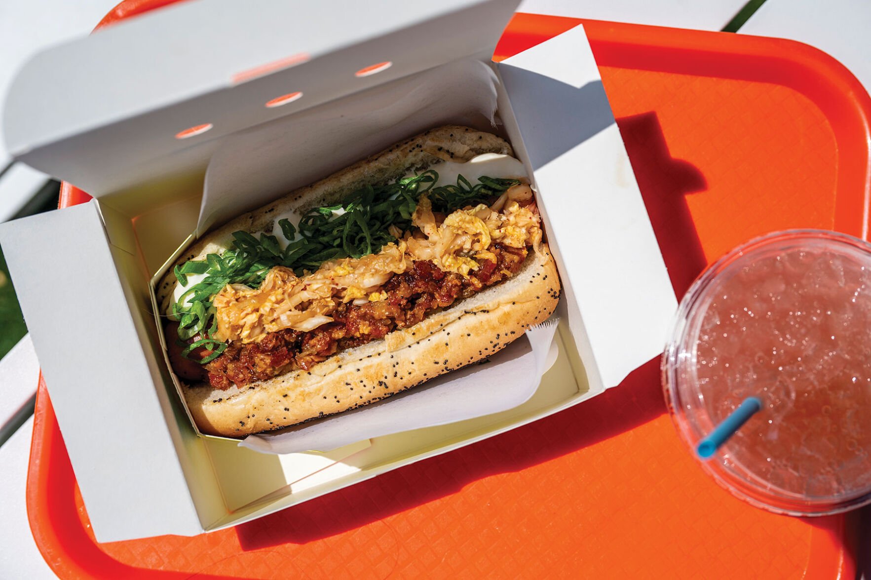 A hot dog with poppy-seed bun, loaded with bacon, cabbage, green onion and more