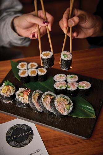 Two hands pick up sushi rolls with chopsticks