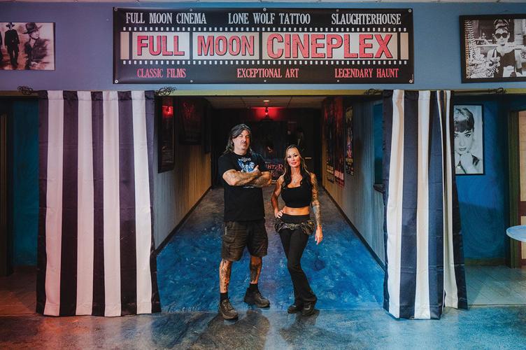 The owners of Full Moon Cineplex stand under a sign bearing the theater's name, stylized as old film, and in front of a hallway leading to a theater.