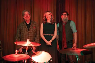 The Ornaments press photo the trio is dressed in Yuletide garb and stands onstage by a drum kit
