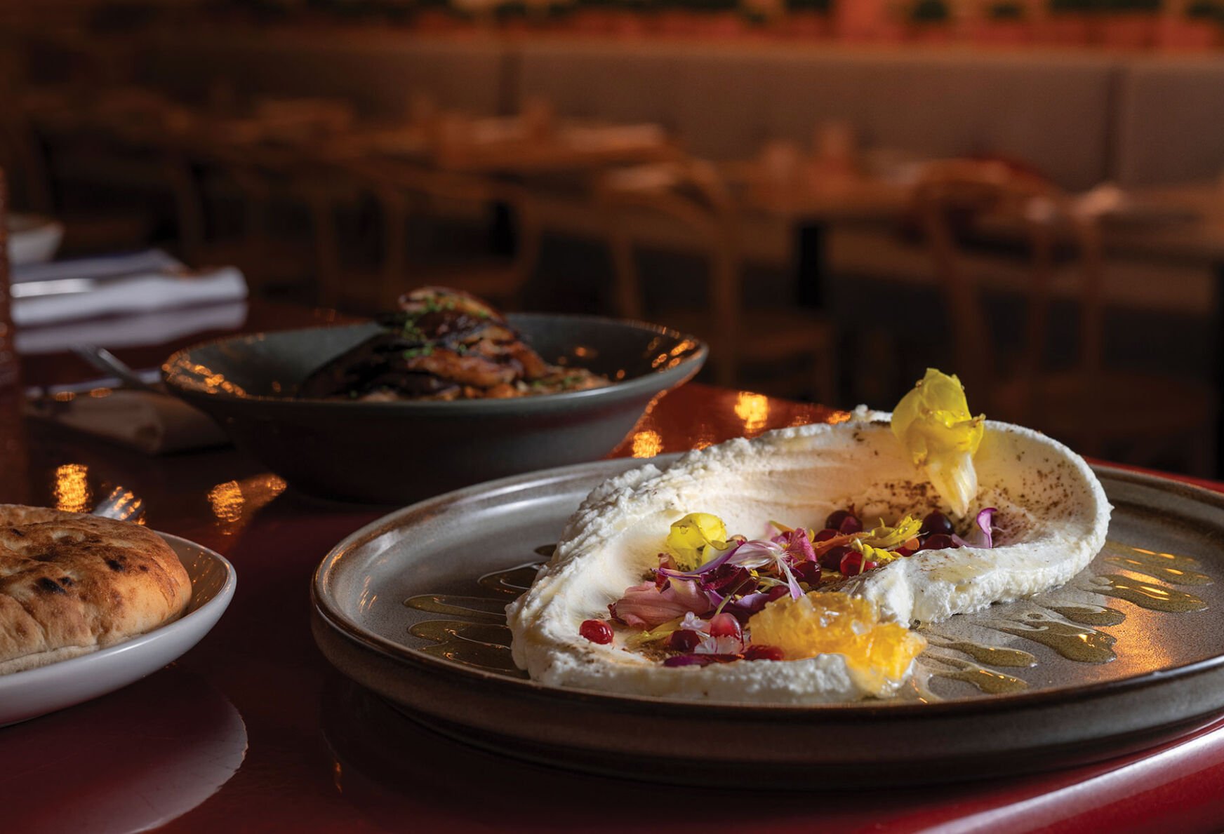 A plate of creamy feta cheese topped with vegetables next to other plates