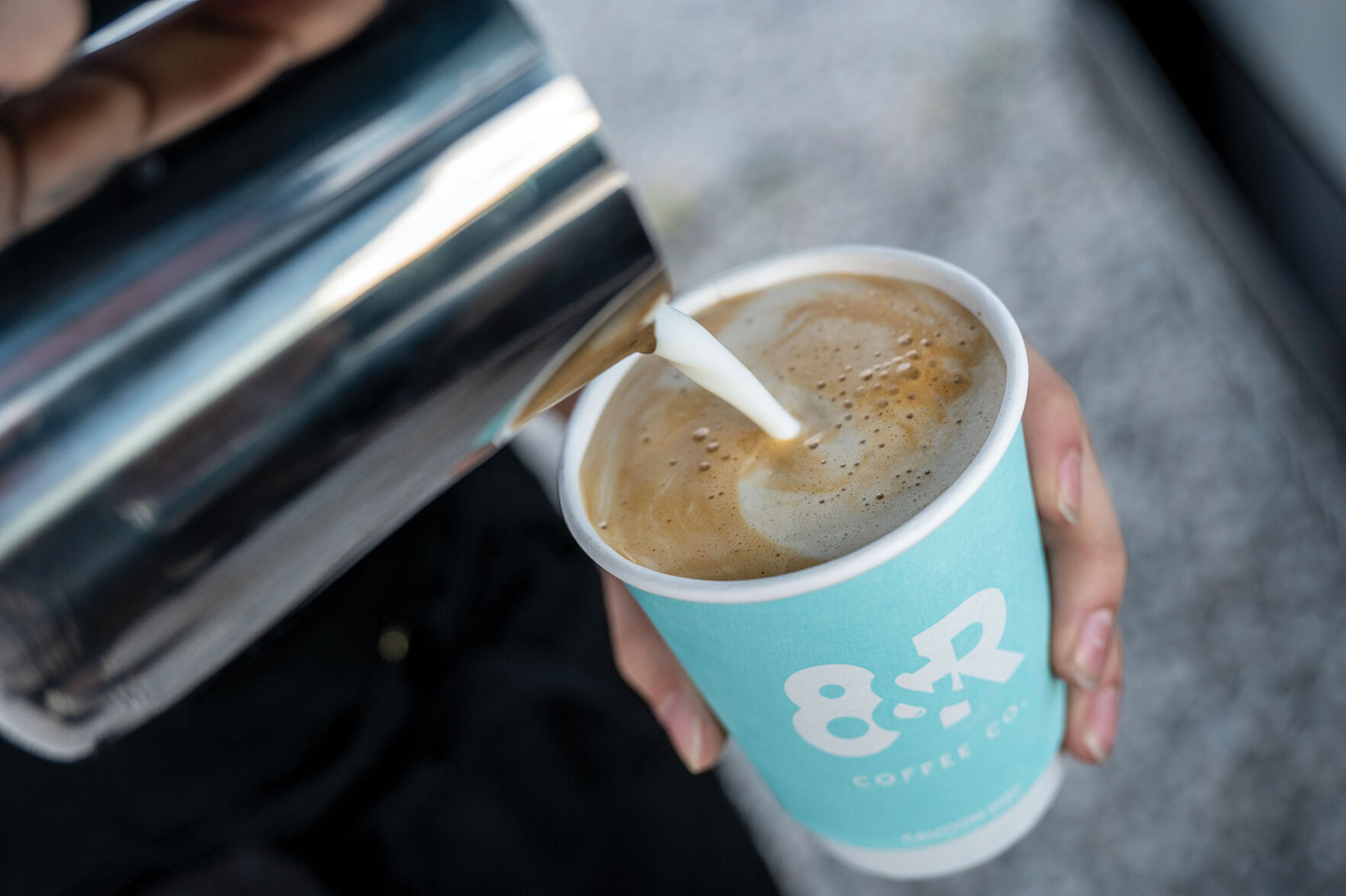Cream being poured into a blue paper cup of coffee