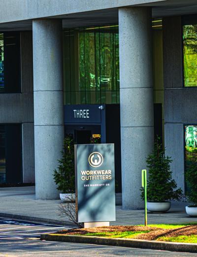 A rectangular sign in front a of a building reads "Workwear Outfitters 545 Marriott Drive." The building behind it features stone columns and tall glass windows.
