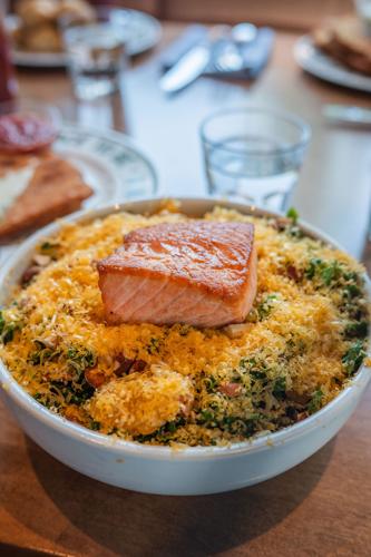 A pink slice of fish on top of a bed of greens and shaved cheese