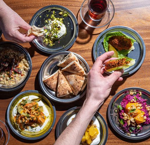 A hand reaches out over seven plates of different Turkish foods. Dishes include hummus, pita and feta.