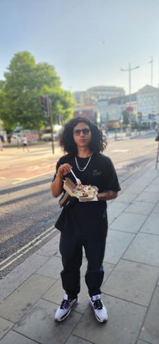 Charly Ortiz-Martinez eats his lunch on a sidewalk his back to an urban street