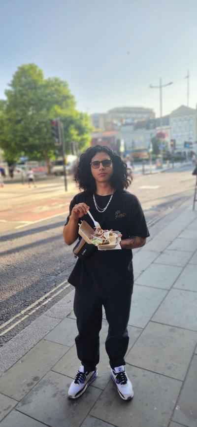 Charly Ortiz-Martinez eats his lunch on a sidewalk his back to an urban street