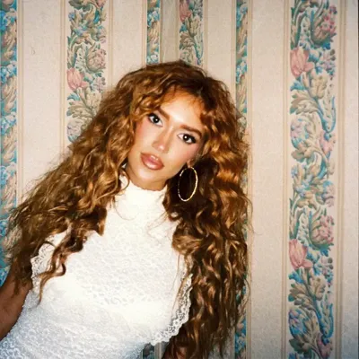 Color press photo of Laci Kaye Booth, the Nashville Scene’s 2026 Best Country Artist, leaning against a wall with stripes of floral print wallpaper