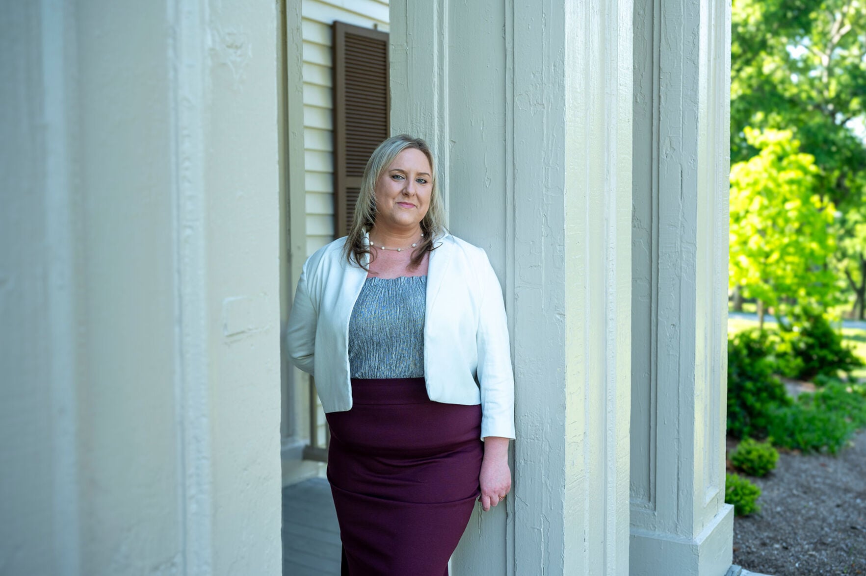 A woman in a white jacket leans against a column outside of a building