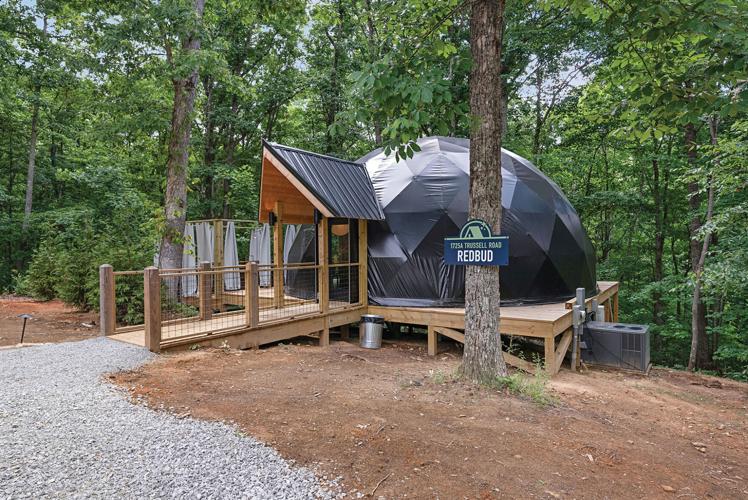 A spherlke cabin covered in a reflective black material on a wooden platform. A sign in front reads "1725A Trussell Road, Redbud."