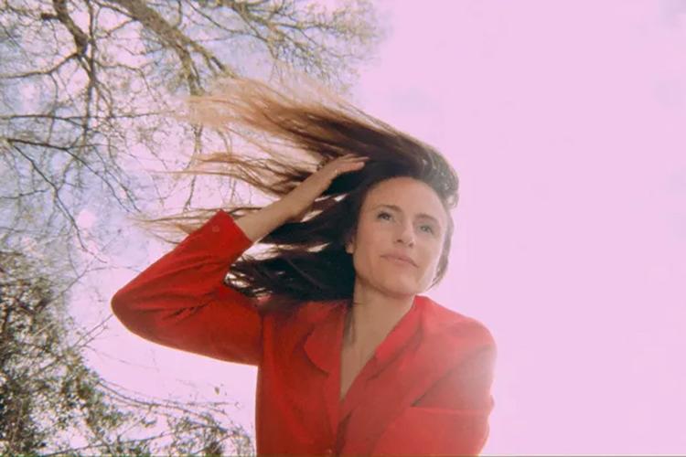 Color press photo of musician Jessie Gray, wearing a red suit jacket as the wind whips her hair to her right.