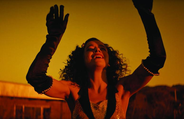 Still from “next in line” featuring a smiling woman with curly hair, raising her hands over her head