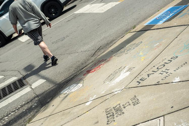 A person walking by graffiti on the sidewalk advertising a music venue