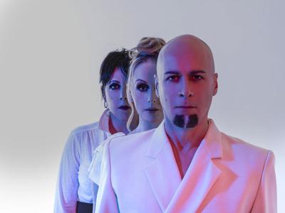 Color press photo from the 2020s in which the three current members of English synth-pop group The Human League stand behind and slightly to the side of each other, so you can only see the right eye of the two members standing behind Phil Oakey.
