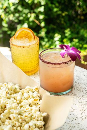 A bright orange drink and light pink drink  in tumblers rest near a basket of popcorn