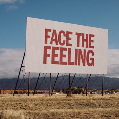 Album art for Jobi Riccio’s second full-length ‘Face the Feeling,’ depicting the title written in red capital letters across a white billboard in a rural area.