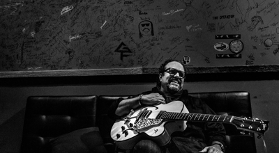 Raul Malo press photo artist sits on a couch in the graffitied green room of a concert venue