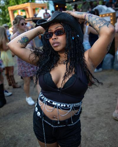 Color street style portrait of CMA Fest fan Mickeda Frankie, in an all-black halter top and shorts with an array of silver accessories topped by a cowboy hat and sunglasses.