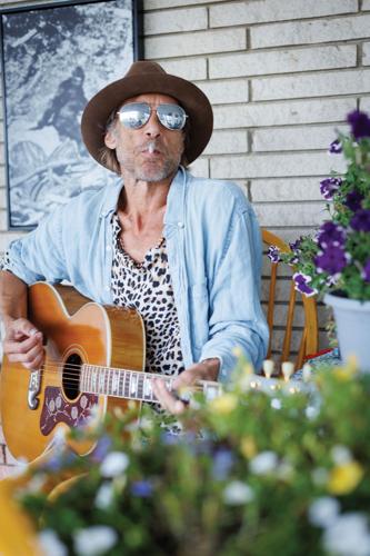 Todd Snider press photo artist plays acoustic guitar on a porch surrounded by flowers