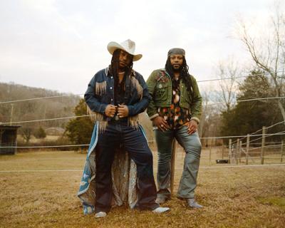 Looking into the camera, artists stand in a field clad in denim Western stagewear