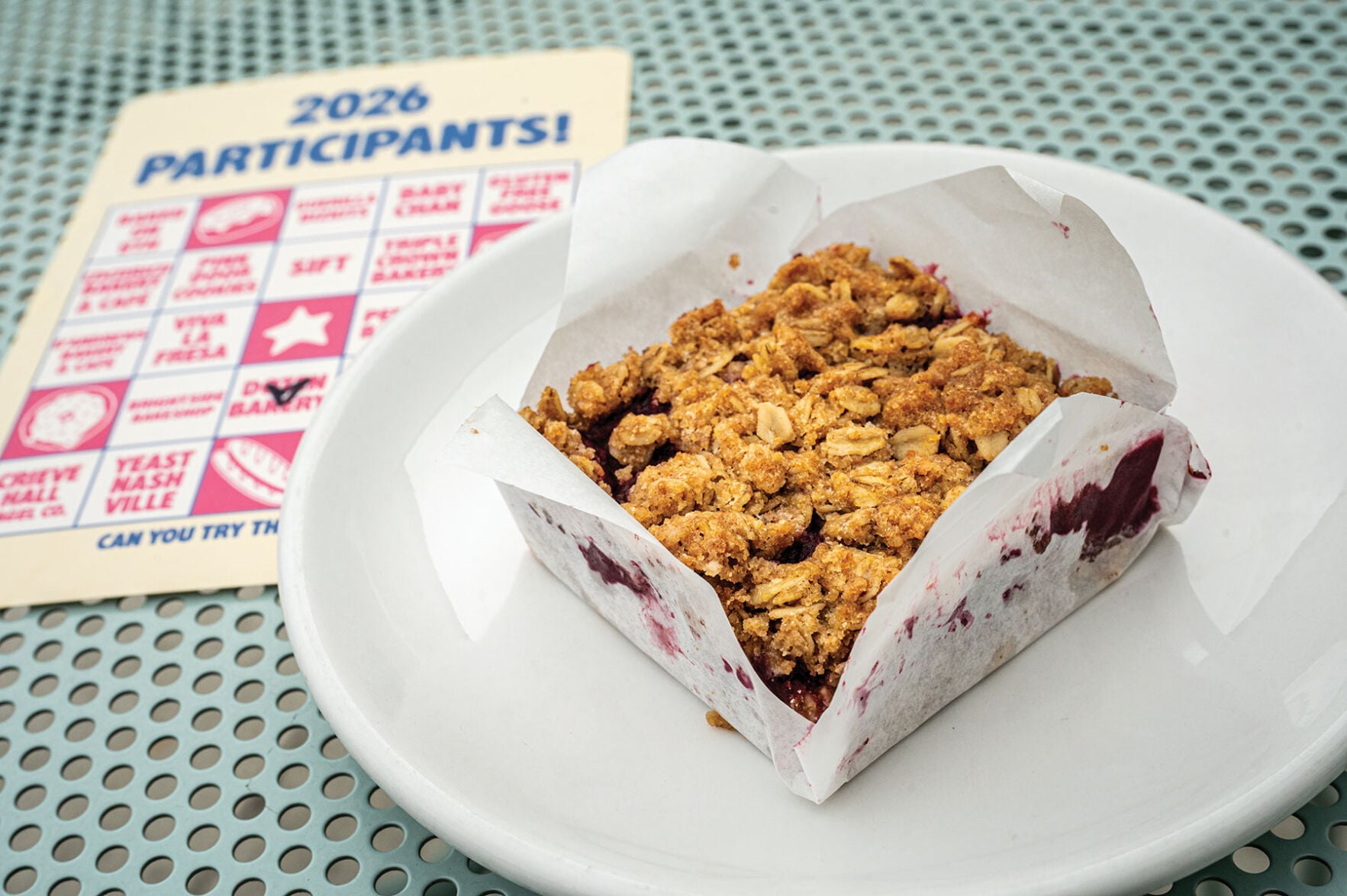 A square pastry on a mesh table next to a bingo card of restaurants participating in a bakery crawl