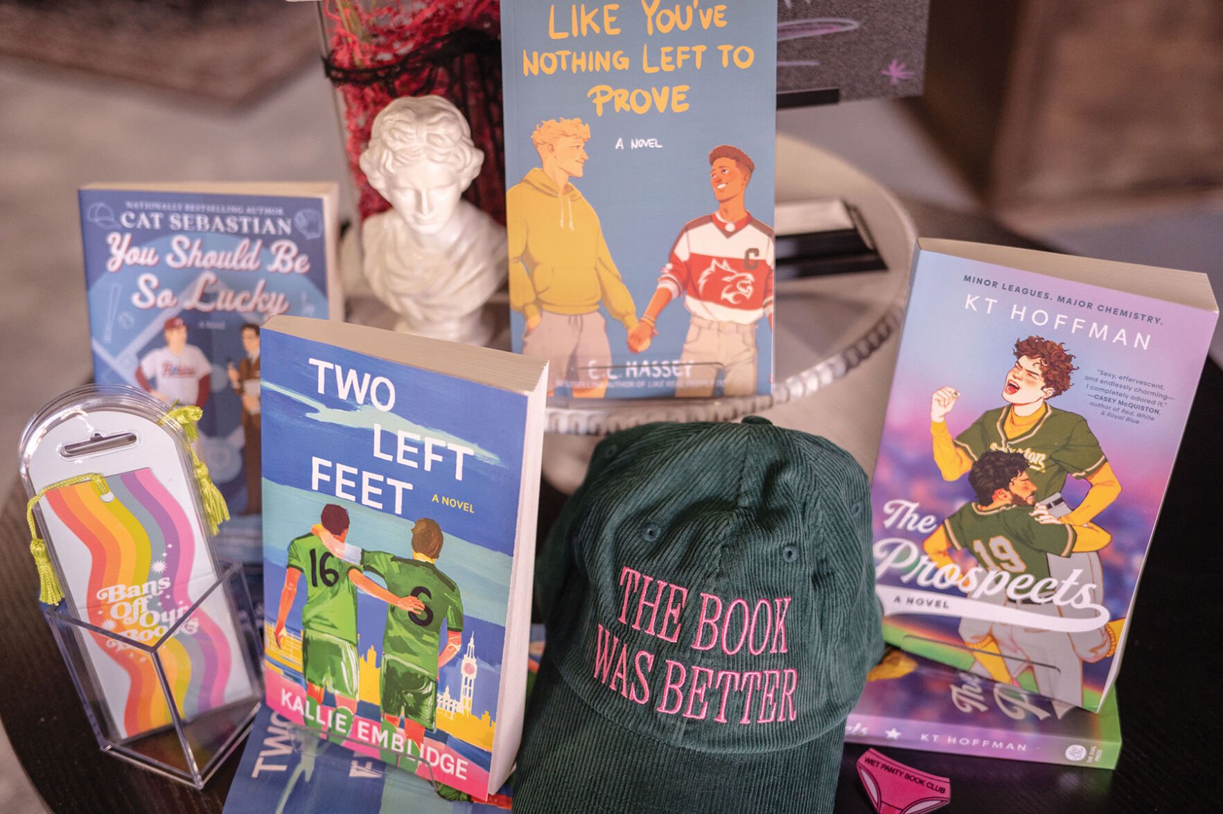A Heated Rivalry-themed display of queer sports romance novels and a hat that reads "The Book Was Better" at Slow Burn