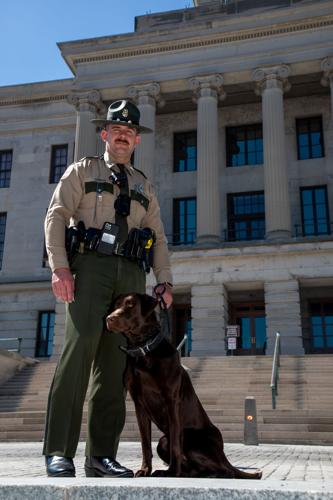 State trooper Brandon Wehrle and K-9 Choco, a 2-year-old chocolate lab trained to sniff for explosives on the steps of the state Capitol, March 19, 2026