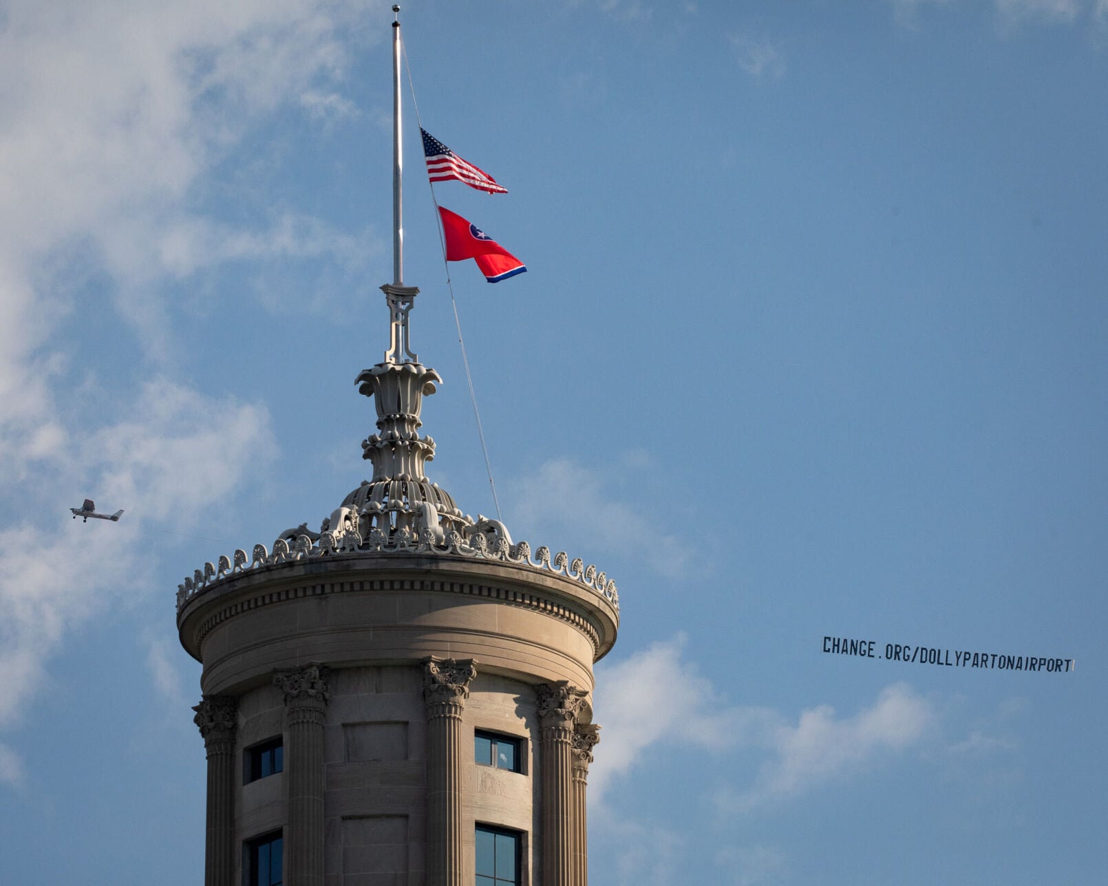 A plane towing a banner promoting a petition to rename the Nashville International Airport in honor of Dolly Parton flies past the state Capitol, Aug. 28