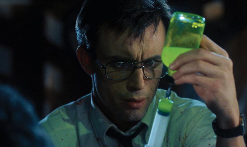 A man with glasses fills a syringe with a strange green fluid, from the film Re-Animator