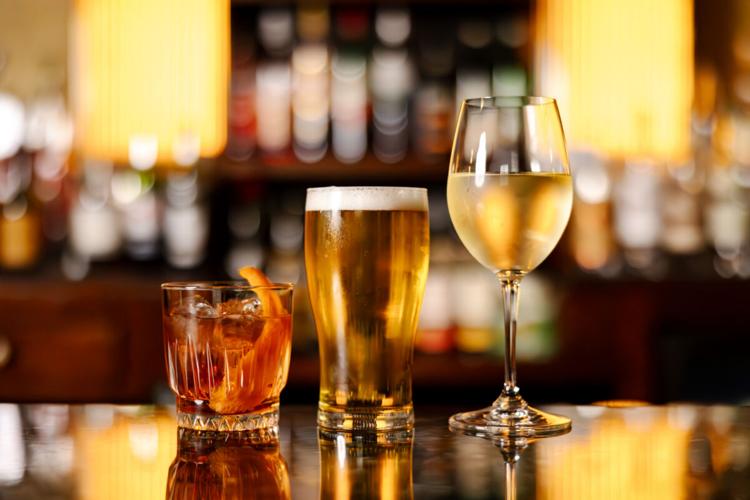 A cocktail, pint of beer and glass of wine lined up on a bar