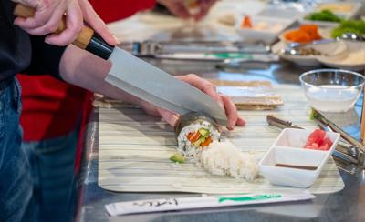 A knife slices a roll of sushi into smaller pieces