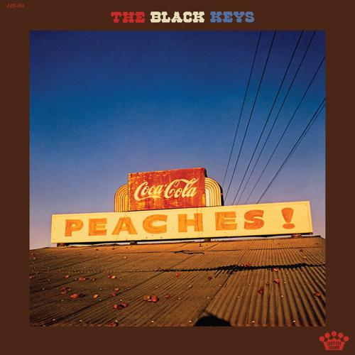 Album art for The Black Keys’ ‘Peaches!,’ consisting of a color photograph of a tin roof with a hand-lettered sign reading “Peaches!” at the crown and peaches scattered about as if they’ve been thrown on the roof.